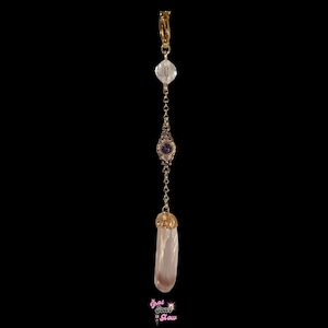 May include: A gold-colored earring with a clear crystal bead, a purple gem, and a pink crystal pendant. The earring is suspended from a gold-colored hoop. The words "That Soul Glow" are at the bottom.