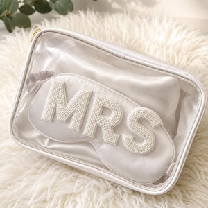 Könnte beinhalten: Eine weiße Schlafmaske aus Satin mit den Buchstaben MRS aus weißen Perlen, verpackt in einer rechteckigen, durchsichtigen Kunststofftasche mit Reißverschluss und weißem Rand. Die Schlafmaske hat ein passendes weißes elastisches Band.