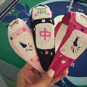 Puede incluir: Tres diademas con cuentas en rosa, negro y fucsia. Cada diadema presenta un dise&ntilde;o central con cuentas blancas y detalles coloridos. La diadema negra tiene un car&aacute;cter chino. Las diademas rosa y fucsia tienen otros dise&ntilde;os.