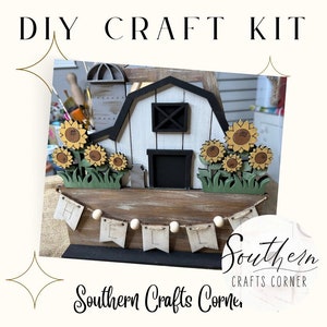 Puede incluir: Kit de manualidades DIY con un granero de madera pintado en blanco y negro, una pancarta de 'Hola' con banderas de madera y un grupo de girasoles. El kit es de Southern Crafts Corner.