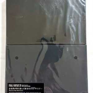 Puede incluir: Una caja de plástico negro con una cubierta de plástico transparente. La caja tiene una etiqueta con el texto "FINAL FANTASY XV Original Soundtrack" y "全世界が待ち望んだ新世代のFFサウンドー Music by Yoko Shimomura".
