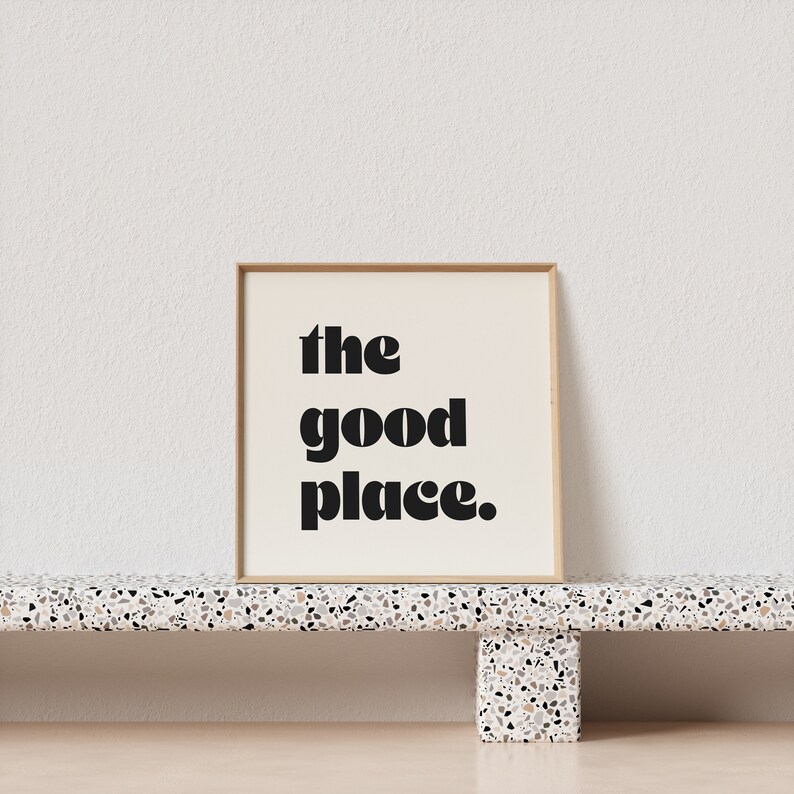 May include: A framed print with a white background and black text that reads "the good place."