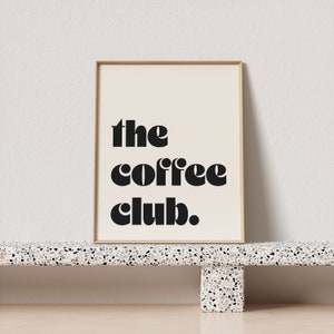 May include: A framed print with the text "the coffee club." in black bold letters on a white background.