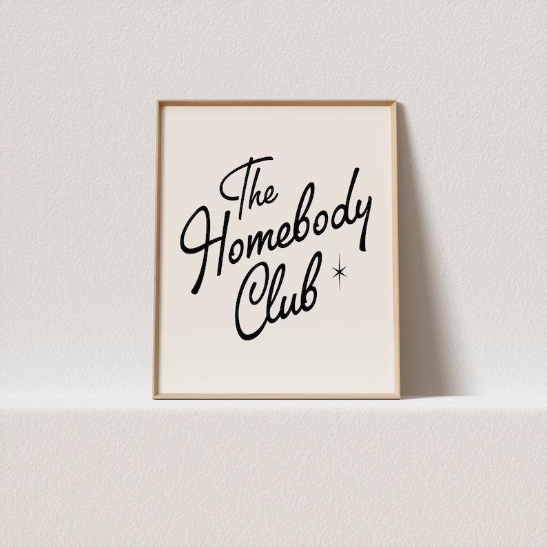 May include: A framed print with a white background and black text that reads "The Homebody Club" with a small star next to the word "Club".