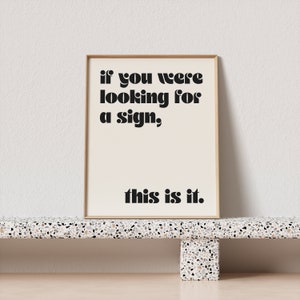 May include: A framed print with a beige background and black text that reads "if you were looking for a sign, this is it."