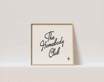 May include: A framed print with a white background and black text that reads "The Homebody Club" with a small star in the bottom right corner.