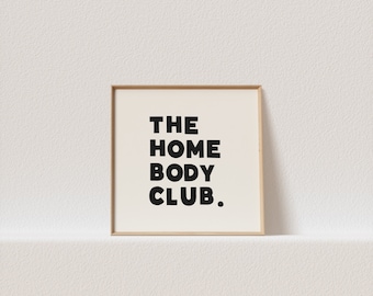 May include: A framed print with the text "THE HOME BODY CLUB." in black bold letters on a white background.