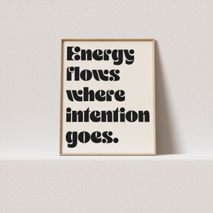 Op de afbeelding: Een ingelijst print met de tekst "Energy flows where intention goes." in zwarte vetgedrukte letters op een witte achtergrond.