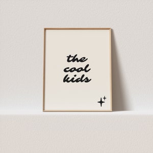 May include: A framed print with the text "the cool kids" in black cursive font on a white background. There are two small black stars in the bottom right corner.