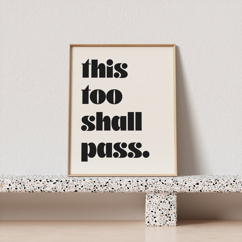 K&ouml;nnte beinhalten: Ein gerahmter Druck mit dem Text "this too shall pass." in schwarzen Fettdruck auf cremefarbenem Hintergrund.