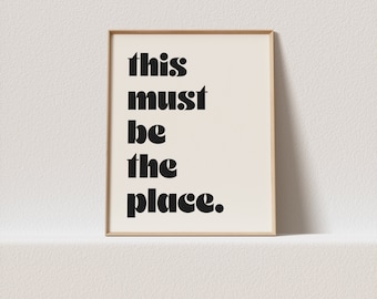 May include: A framed print with the text "this must be the place." in black bold letters on a white background.