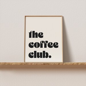 May include: A framed print with the text "the coffee club." in black bold letters on a white background.