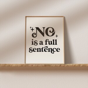 May include: A framed print with the words "NO is a full sentence" in a black, retro-style font. The print has a cream-colored background and is set in a light brown frame. The print is displayed on a wooden shelf.