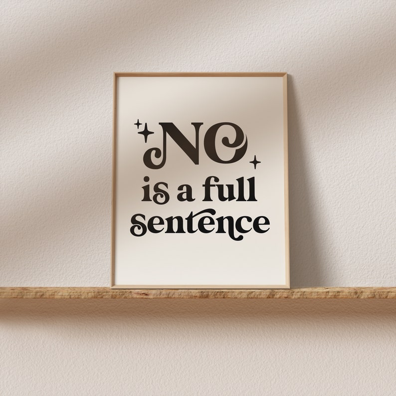 May include: A framed print with the words "NO is a full sentence" in a black, retro-style font. The print has a cream-colored background and is set in a light brown frame. The print is displayed on a wooden shelf.