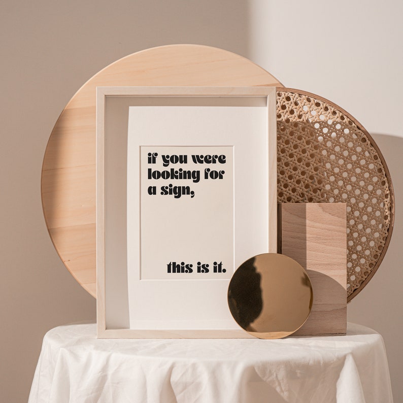 May include: A white framed print with the text "if you were looking for a sign, this is it." The print is sitting on a white table with a wooden tray and a woven basket behind it.