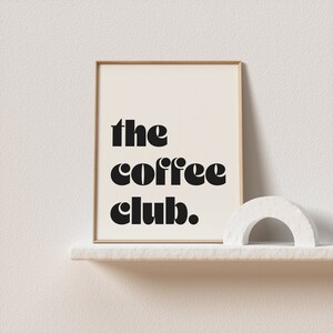 May include: A framed print with the text "the coffee club." in black bold letters on a white background.
