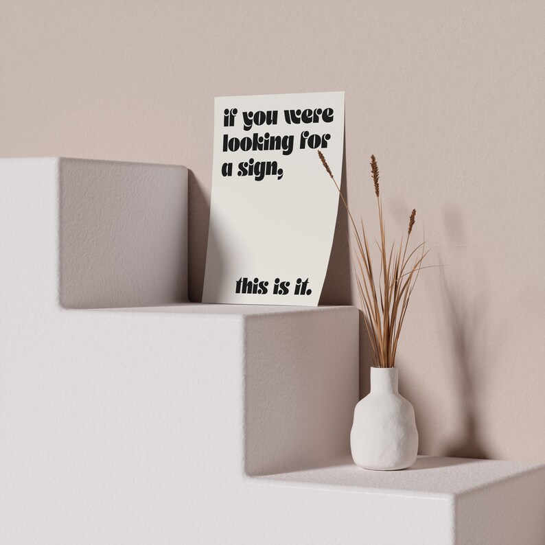 May include: A white card with black text that reads "if you were looking for a sign, this is it." The card is sitting on a white shelf with a white vase with dried brown grass on the right side.