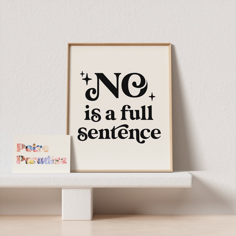 May include: A framed print with the words "NO is a full sentence" in black script. A smaller card with the words "Poise Paradise" in colorful letters is in front of the print. The background is a neutral color.