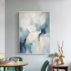 May include: Abstract painting with blue and white geometric shapes on a canvas. The painting is framed in a white frame and is hanging on a light gray wall.