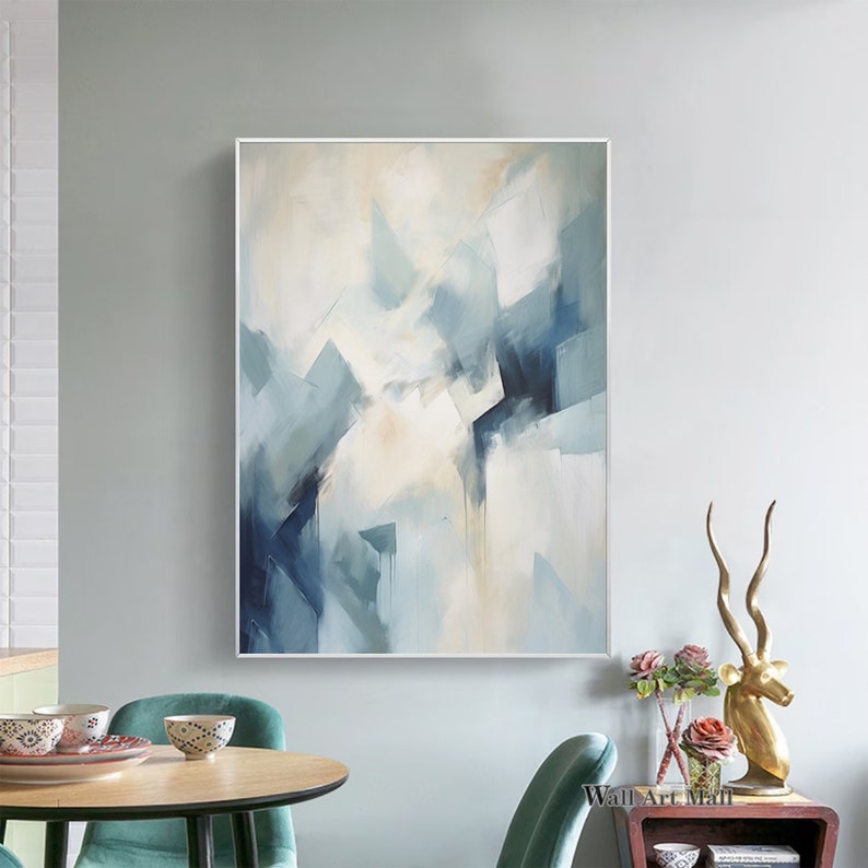 May include: Abstract painting with blue and white geometric shapes on a canvas. The painting is framed in a white frame and is hanging on a light gray wall.