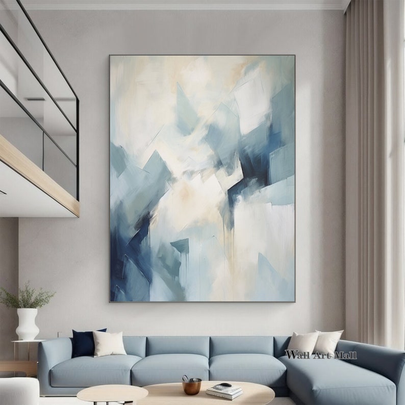 May include: Abstract painting with a white background and blue and gray geometric shapes. The painting is hanging on a wall in a living room setting.