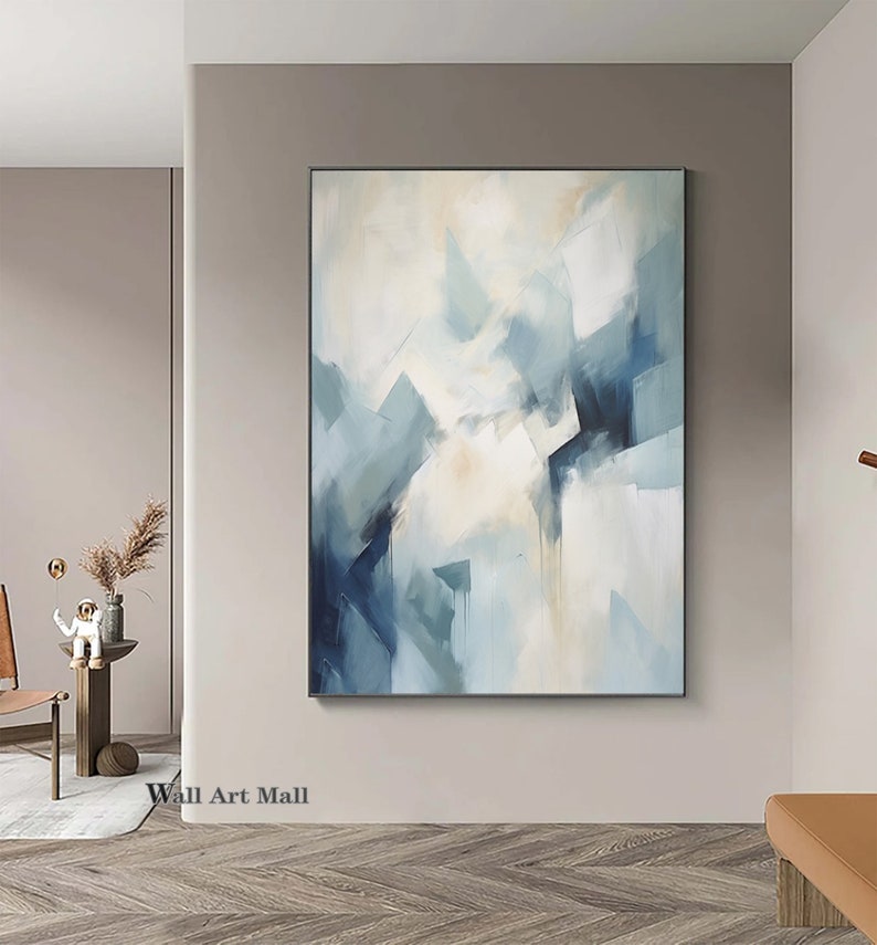 May include: Abstract painting with a white background and blue and gray geometric shapes. The painting is framed and hanging on a wall.