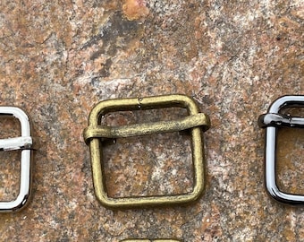 May include: Three metal belt buckle slides in different finishes: silver, brass, and black.