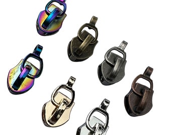May include: Assortment of seven zipper pulls in various finishes, including gold, silver, bronze, and iridescent. Each pull features a shield-shaped design with a loop at the top.