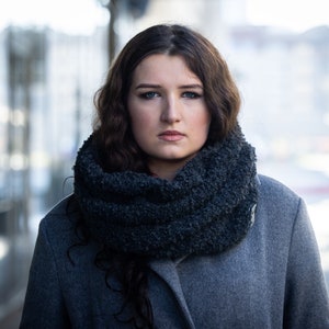 Könnte beinhalten: Eine Frau mit langen braunen Haaren trägt einen grauen Mantel und einen dunkelgrauen, flauschigen Schal. Sie schaut direkt in die Kamera.