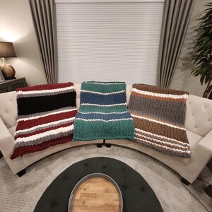 Peut inclure: Trois couvertures en tricot &eacute;pais de couleurs vari&eacute;es sont pos&eacute;es sur un canap&eacute; blanc. L'une pr&eacute;sente des rayures bordeaux, blanches et grises. Une autre a des rayures vertes et bleues. La troisi&egrave;me a des rayures marron, grises et blanches.
