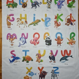 May include: White fabric featuring the alphabet with colorful letters and corresponding animal illustrations. Each letter has a unique animal, such as an alligator for A, a bee for B, and a zebra for Z. The fabric is suitable for educational purposes.