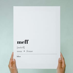 May include: A white rectangular canvas with the word "meff" in a bold, black font. Below, the phonetic pronunciation, part of speech, and a definition: "Idiot." The canvas is held by two hands against a light green background.