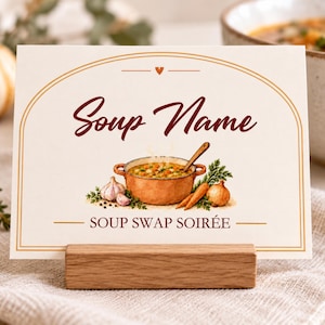 May include: A rectangular cream-colored card with a brown arched border, featuring the text Soup Name and SOUP SWAP SOIRÉE. The center displays a watercolor illustration of a copper pot filled with soup, garlic, carrots, and an onion.