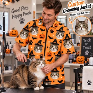 Könnte beinhalten: Eine orangefarbene kurzärmelige Pflegejacke mit einem sich wiederholenden Muster aus Katzengesichtern mit schwarzen Hexenhüten, Kürbissen, schwarzen Fledermäusen und Pfotenabdrücken. Die Jacke verfügt über einen Reißverschluss vorne.