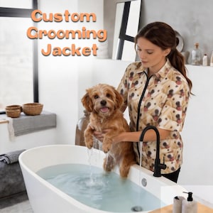 Könnte beinhalten: Eine Frau trägt eine maßgeschneiderte Pflegejacke mit einem Muster aus Golden Retriever-Gesichtern und hält einen kleinen, nassen, braunen Hund in einer weißen Badewanne. Der Text "Custom Grooming Jacket" ist orange.