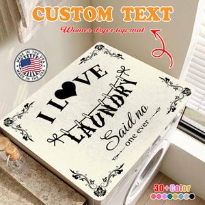 May include: A cream-colored laundry mat with the text "I LOVE LAUNDRY Said no one ever" in black. The mat has a heart and decorative corner designs. The mat is placed on top of a washing machine.