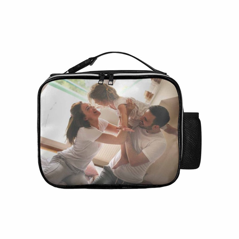 May include: Black lunch bag with a zipper closure and a side pocket. The bag features a printed image of a family of three, a woman, a man, and a child, playing together.