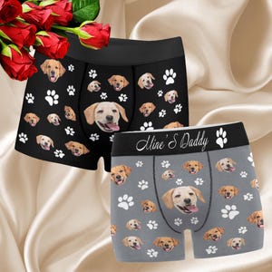 May include: Two pairs of boxer shorts with a dog print. One pair is black with white paw prints and the other is gray with white paw prints. The gray pair has the text "Mine's Daddy" on the waistband.