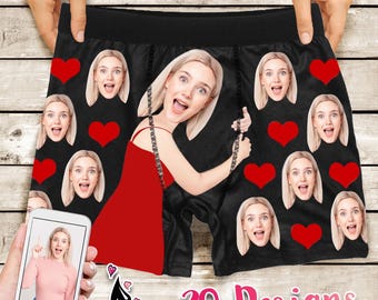 May include: Black boxer shorts with a repeated pattern of red hearts and a woman's face. The woman's face is partially obscured by a red dress.
