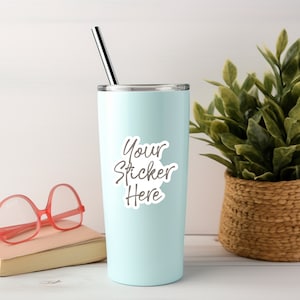 May include: A light blue stainless steel tumbler with a white sticker that says "Your Sticker Here". The tumbler has a silver lid and a silver straw.