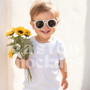 May include: A young child wearing white sunglasses and a white t-shirt holds a bouquet of yellow sunflowers.