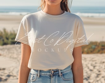 May include: A woman wearing a light beige t-shirt with a crew neck and short sleeves. The t-shirt is blank and ready for customization. The woman is standing on a sandy beach.