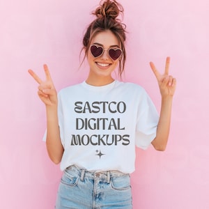 May include: A white t-shirt with the text "EASTCO DIGITAL MOCKUPS" printed in gray on the front. The model is wearing the shirt and smiling at the camera.