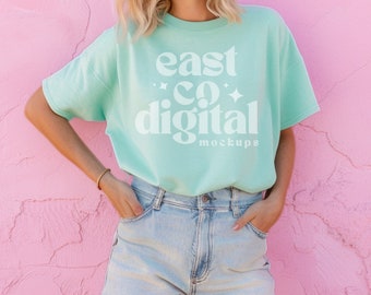 Puede incluir: Una camiseta azul claro con el texto "east co digital mockups" en blanco. La camiseta la lleva puesta una persona con el pelo rubio y se combina con unos pantalones cortos de mezclilla.