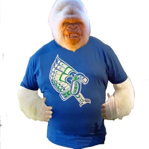 May include: A white gorilla wearing a blue t-shirt with a green, white, and blue eagle design. The eagle is flying with its wings spread.