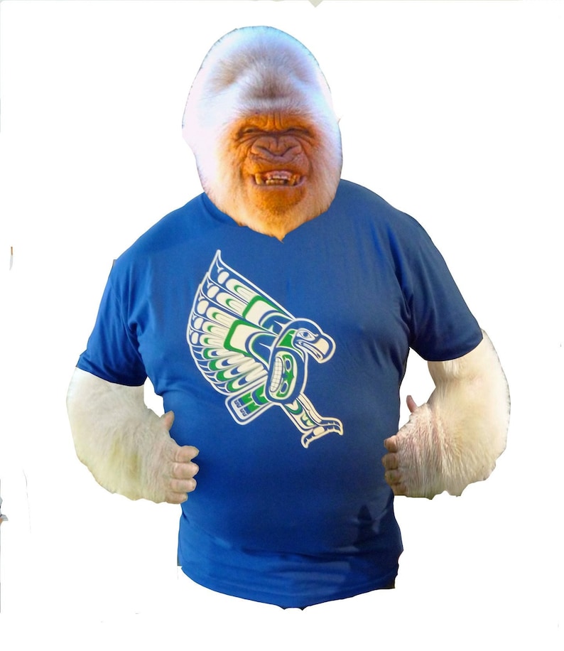 May include: A white gorilla wearing a blue t-shirt with a green, white, and blue eagle design. The eagle is flying with its wings spread.