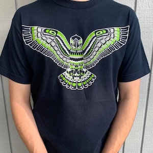 May include: A black t-shirt with a green and white stylized graphic of a bird with outstretched wings.