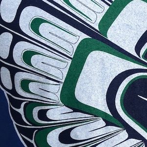 May include: A close-up of a blue and white fabric with a green and black design. The design is a stylized pattern of feathers or wings.