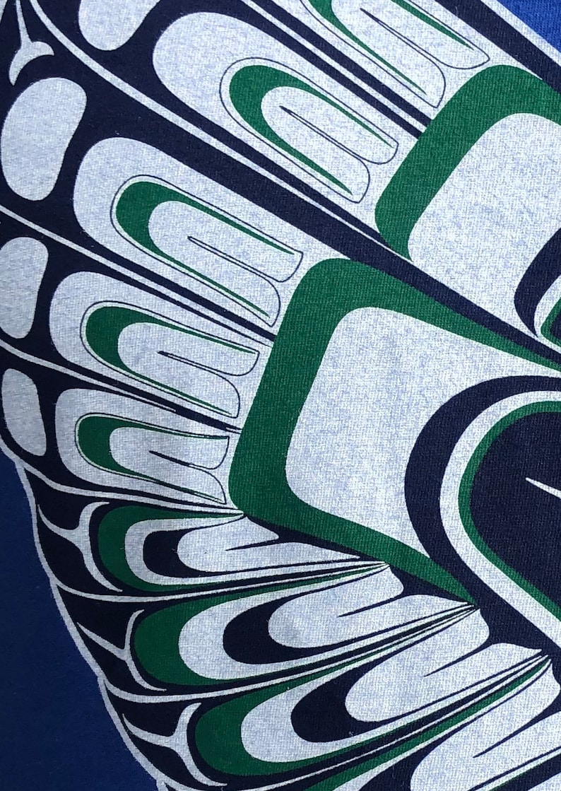 May include: A close-up of a blue and white fabric with a green and black design. The design is a stylized pattern of feathers or wings.