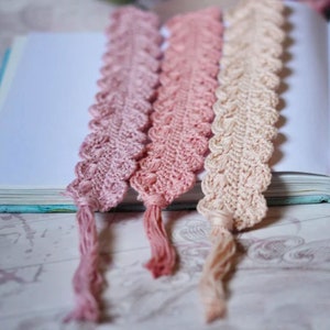 Könnte beinhalten: Drei gehäkelte Lesezeichen in Rosatönen mit zarten gewellten Kanten und Quasten.